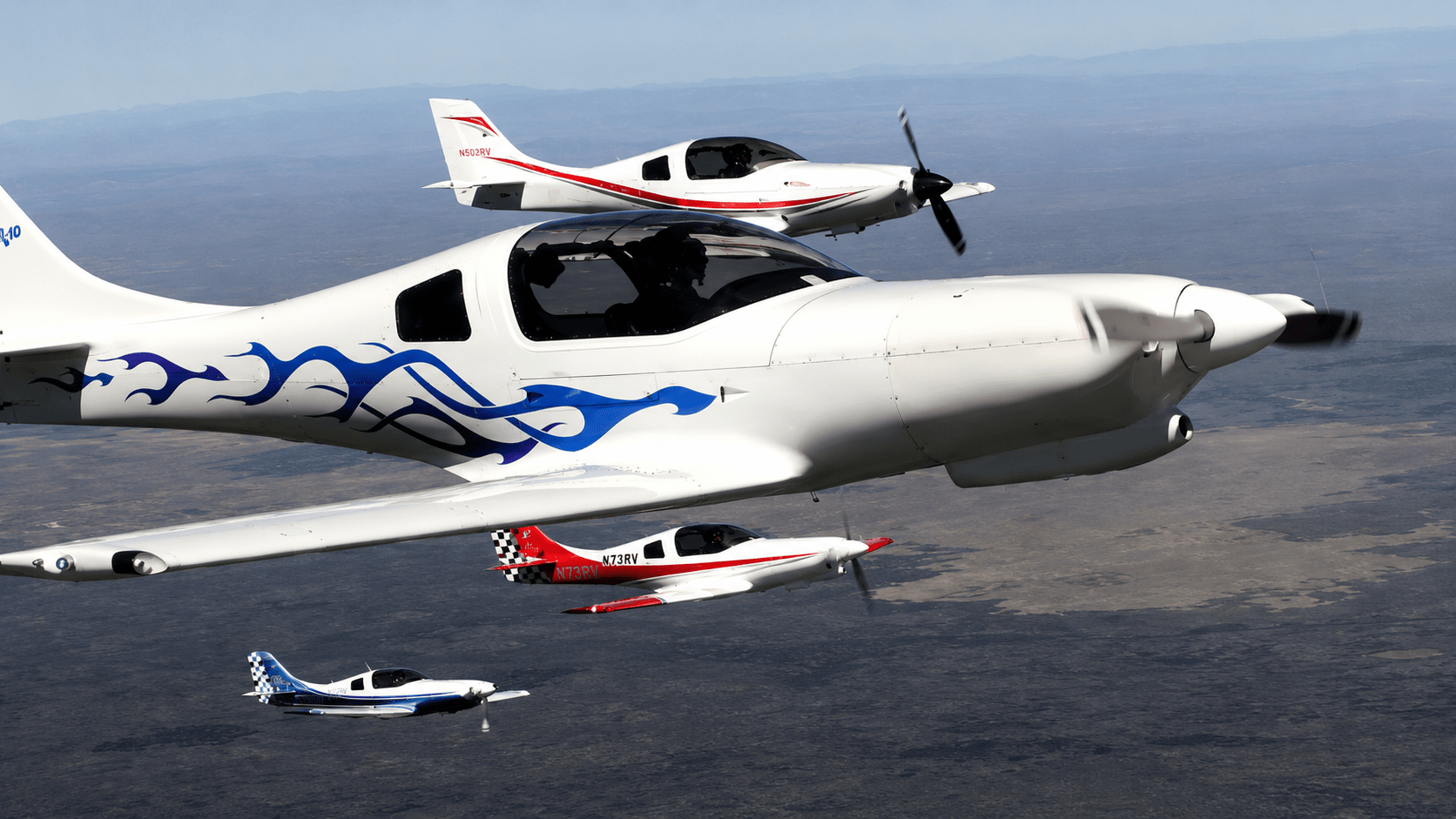 Three Lancair aircraft flying in tight formation over open terrain